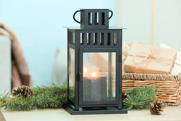 Yanan mumlu fener, köknar dalları ve masada Noel hediyeleri.