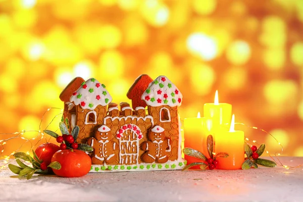 Zencefilli kurabiye evi, mandalinalar ve yanan mumlar bulanık arka planda.