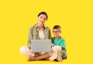 Küçük çocuk ve ablası sarı arka planda dizüstü bilgisayar kullanıyorlar.