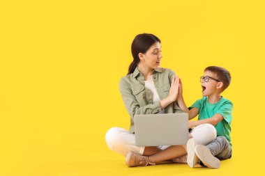 Küçük oğlan ve dizüstü bilgisayarlı ablası sarı arka planda birbirlerine beşlik çakıyorlar.