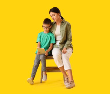 Küçük çocuk ve ablası sarı arka planda tablet bilgisayar kullanıyorlar.