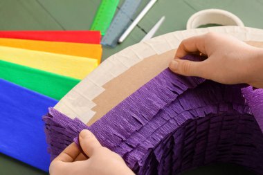 Yeşil ahşap arka planda mor kağıtlı Meksika pinyatası yapan kadın, yakın plan.