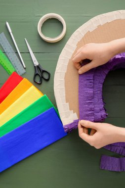 Yeşil ahşap arka planda mor kağıtlı Meksika pinyatası yapan kadın.