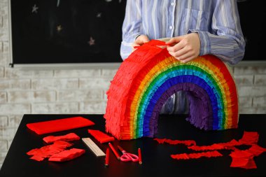 Evdeki masada gökkuşağı şeklinde Meksika pinyatası yapan kadın.