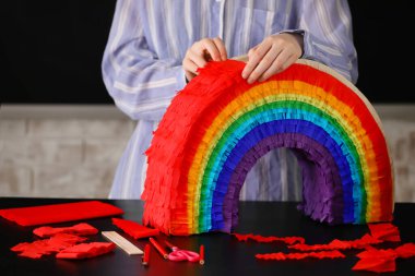Evdeki masada gökkuşağı şeklinde Meksika pinyatası yapan kadın.