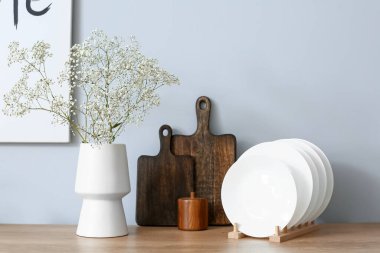 Yeşil çiçekli vazo, levhalar ve tabaklar ışık duvarının yanında.