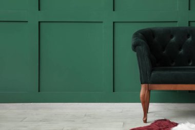 Yeşil duvarın yanında şık koltuğu olan modern bir iç mekan.