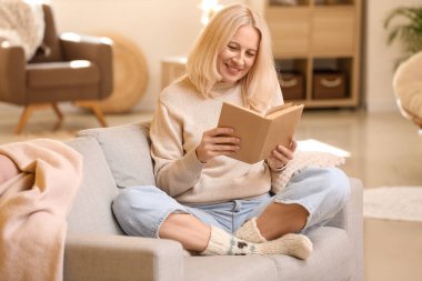 Güz günü evde kitap okuyan güzel olgun bir kadın.