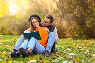 Yeşil çimlerde oturan ve sonbahar parkında kitap okuyan sevgi dolu çift.