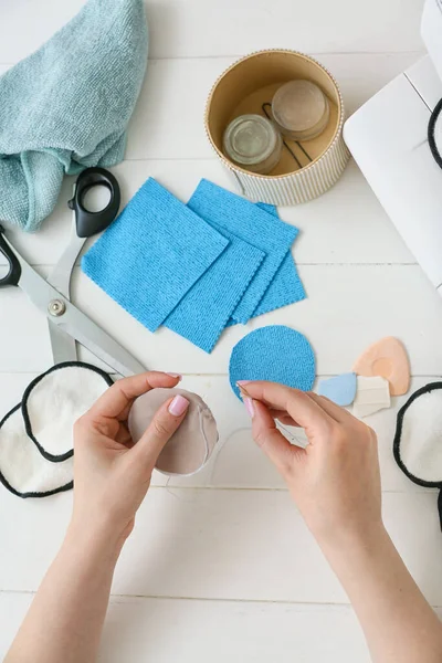 İğnesi olan kadın beyaz ahşap arka planda tekrar kullanılabilir pamuk yastık yapıyor.