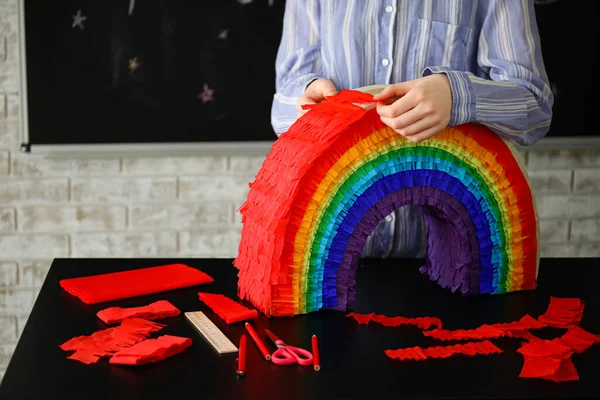 Evdeki masada gökkuşağı şeklinde Meksika pinyatası yapan kadın.