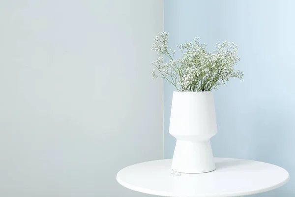Vase with gypsophila flowers on table near light wall