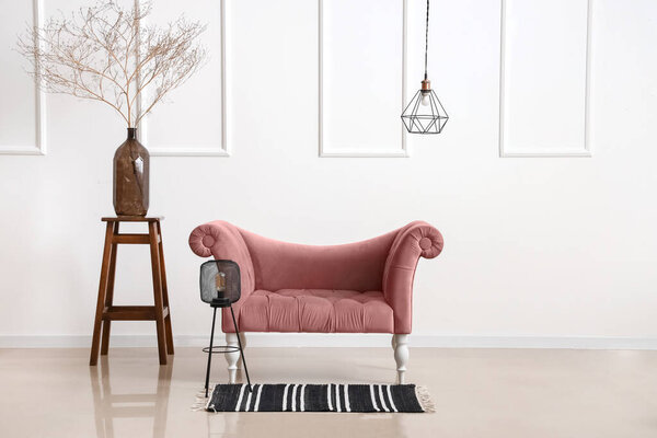 Pink armchair, lamp and vase with branches near light wall