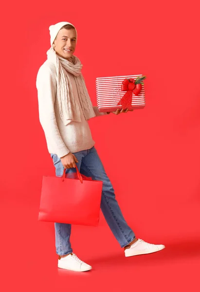 Junger Mann Mit Weihnachtsgeschenk Und Einkaufstasche Auf Farbigem Hintergrund — Stockfoto