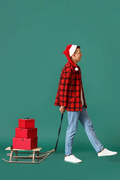 Junger Mann Mit Weihnachtsgeschenken Auf Schlitten Vor Farbigem Hintergrund — Stockfoto