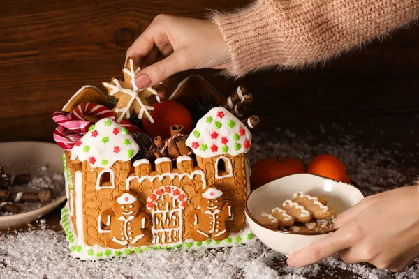 Woman Putting Cookies Gingerbread House Wooden Background — Stock Photo, Image