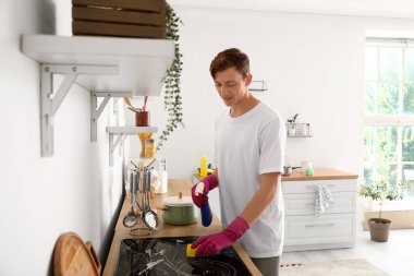 Genç adam mutfakta süngerle sobayı temizliyor.