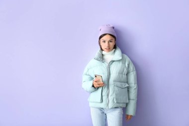 Şık, kalın giysiler içinde ve telefonlu, renkli arka planlı genç bir kadın.