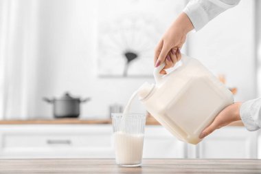 Kadın mutfaktaki masaya bir galon sütü bardağa boşaltıyor.