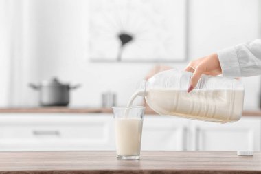 Kadın mutfaktaki masaya bir galon sütü bardağa döküyor.