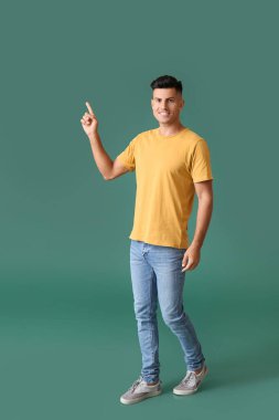 Şık tişörtlü yakışıklı genç adam arka plandaki bir şeyi işaret ediyor.