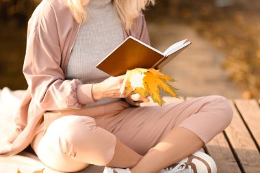 Sonbahar günü nehir kenarında kitap okuyan olgun bir kadın.