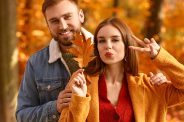 Sonbahar yapraklı genç çift parkta zafer jesti gösteriyor.