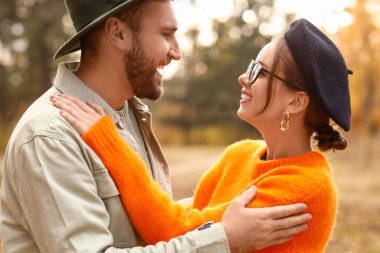 Mutlu genç çift, sonbahar parkında birbirlerine sarılıp bakıyorlar.