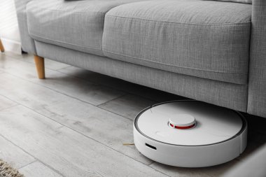 Odadaki kanepenin yanındaki modern robot elektrikli süpürge.