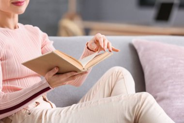 Evdeki kanepede kitap okuyan genç bir kadın, yakın çekim.