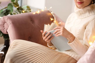 Evdeki kanepede kitap okuyan genç bir kadın, yakın çekim.