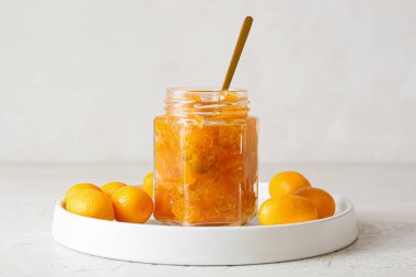 Bir kavanoz lezzetli kumkat reçeli ve hafif arkaplanda taze meyveler.