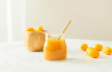 Bir kavanoz lezzetli kumkat reçeli ve hafif arkaplanda taze meyveler.