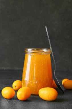 Lezzetli kumkat reçeli kavanozu ve siyah arka planda taze meyveler.