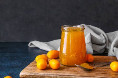Lezzetli kumkat reçeli kavanozu ve siyah arka planda taze meyveler.