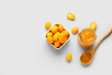 Bir kavanoz lezzetli kumkat reçeli ve beyaz arka planda taze meyveli kase.