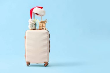 Noel hediyesi kutusu, ahşap uçak, çalar saat, güneş gözlüğü ve mavi arka planda Noel Baba şapkası.