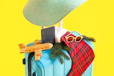 Aksesuarlı mavi bavul, Noel çorabı, tahta uçak ve sarı arka planda pasaport.