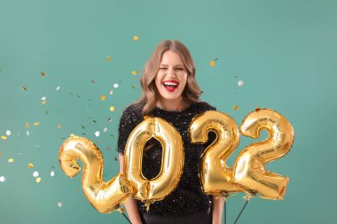 Renkli arka planda 2022 şeklinde balonları olan güzel genç bir kadın. Yeni yıl kutlaması