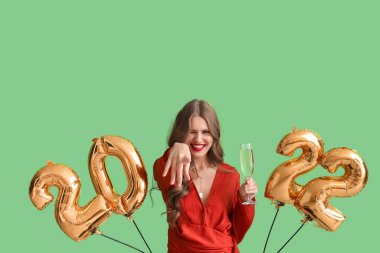 Yeşil arka planda 2022 figüründe şampanya ve balonları olan güzel genç bir kadın. Yeni yıl kutlaması