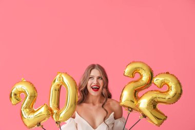 Pembe arka planda 2022 şeklinde balonları olan güzel genç bir kadın. Yeni yıl kutlaması