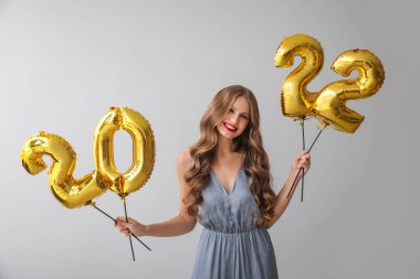 Gri arka planda 2022 şeklinde balonları olan güzel genç bir kadın. Yeni yıl kutlaması