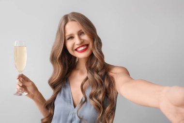 Şampanyalı güzel genç bir kadın gri arka planda selfie çekiyor.