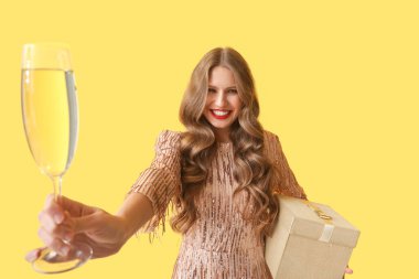 Sarı arka planda hediye ve şampanyası olan güzel genç bir kadın.