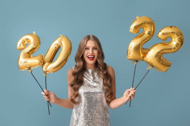 Mavi arka planda 2022 şeklinde balonları olan güzel genç bir kadın. Yeni yıl kutlaması