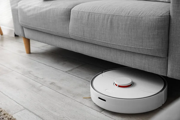 Odadaki kanepenin yanındaki modern robot elektrikli süpürge.