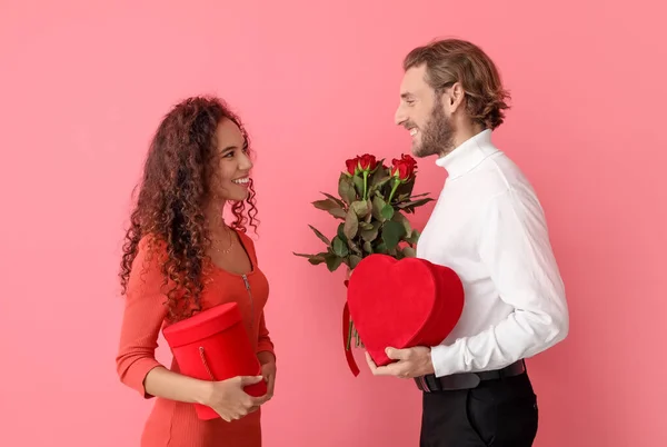色の背景に贈り物や花を持つ幸せな若いカップル バレンタインデーのお祝い — ストック写真