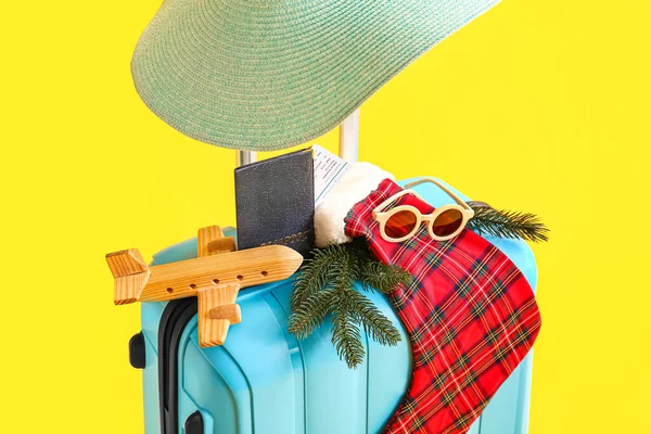 Aksesuarlı mavi bavul, Noel çorabı, tahta uçak ve sarı arka planda pasaport.