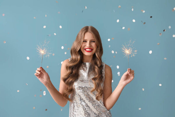Beautiful young woman with sparklers on blue background. New Year celebration