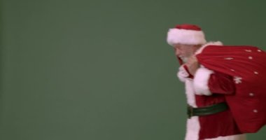 Yürüyen Noel Baba yeşil arka planda el sallıyor.